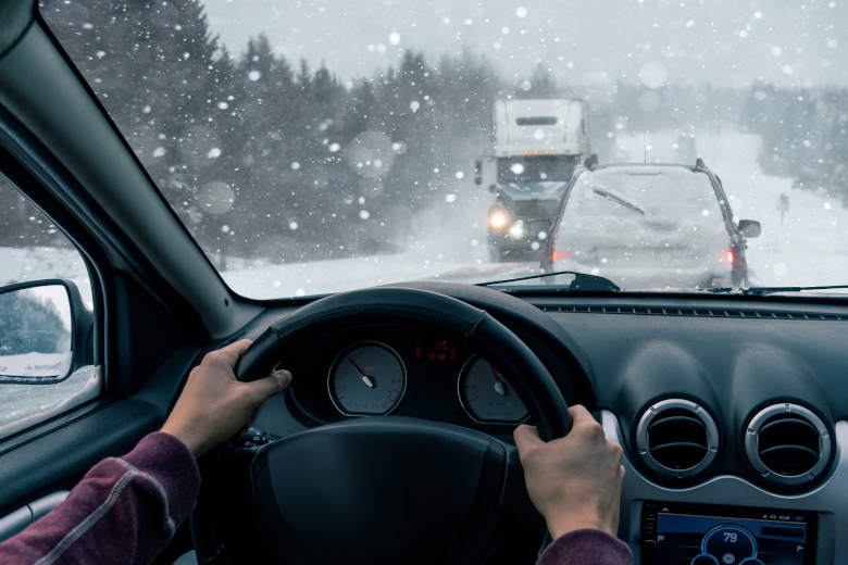 Perspective from the back seat inside a car with a man driving on a busy, snowy road