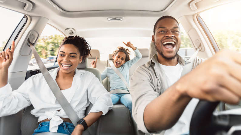 Happy black family of three singing and having fun riding in a car