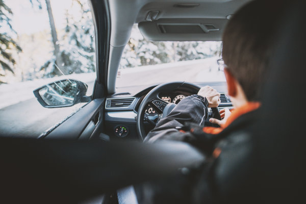 Rear view from the car of a young man driving on a snowy winter day.